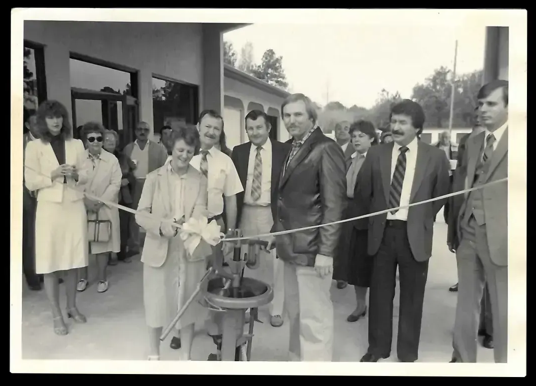 People cutting a ribbon at a building's opening. A crowd watches.