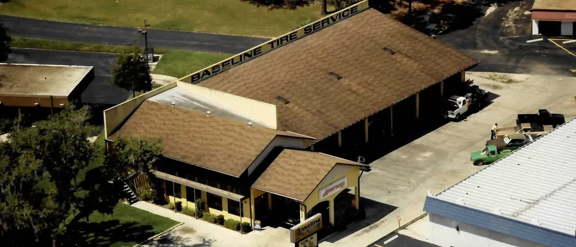 Aerial view of a brown-roofed building and surrounding area with vehicles and trees.