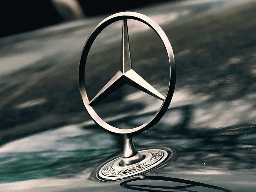 Mercedes-Benz hood ornament; silver three-pointed star in a circle atop a vehicle's hood, reflecting the surroundings.