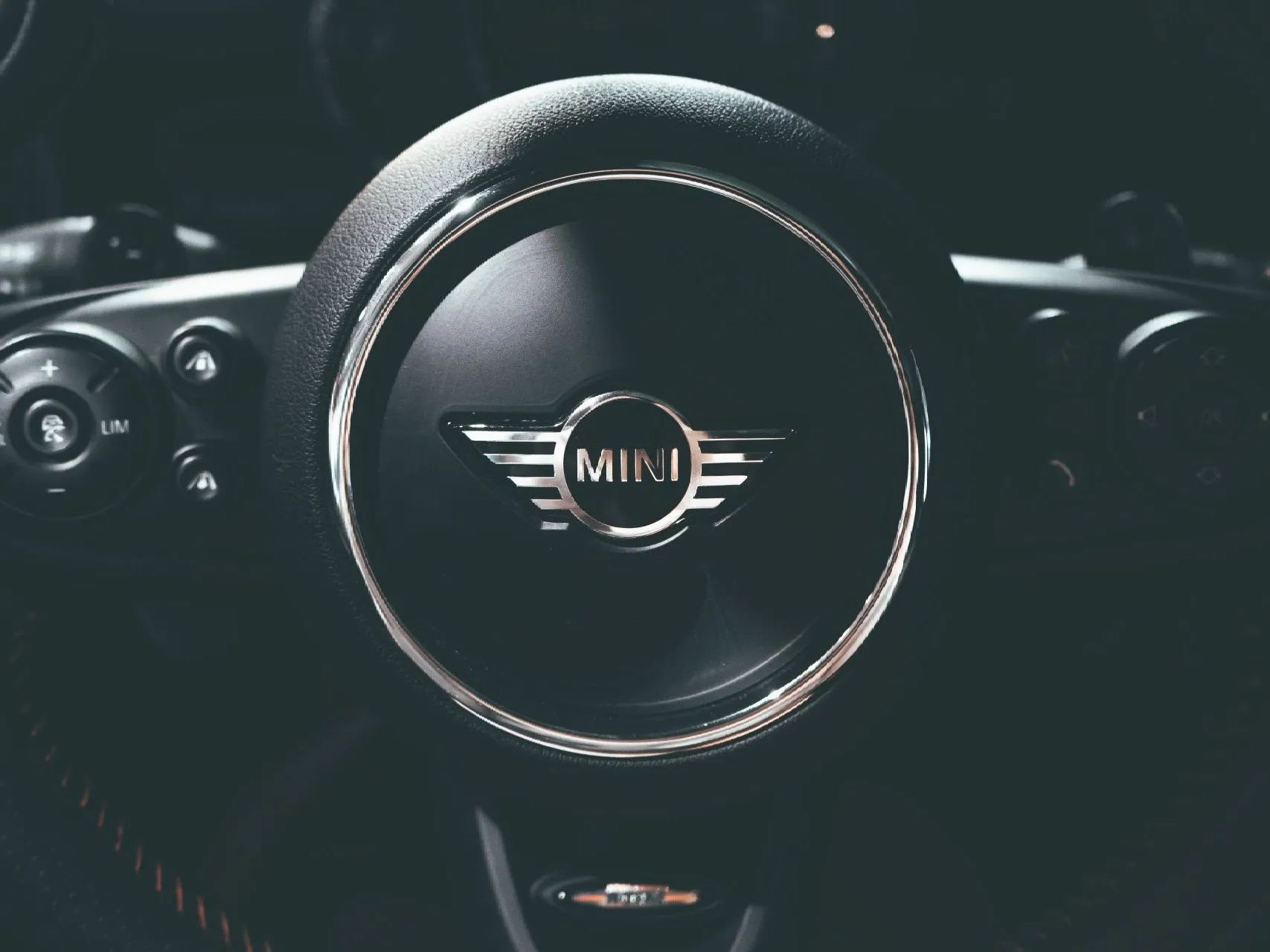 Close-up of a Mini Cooper steering wheel, black with a silver MINI logo.