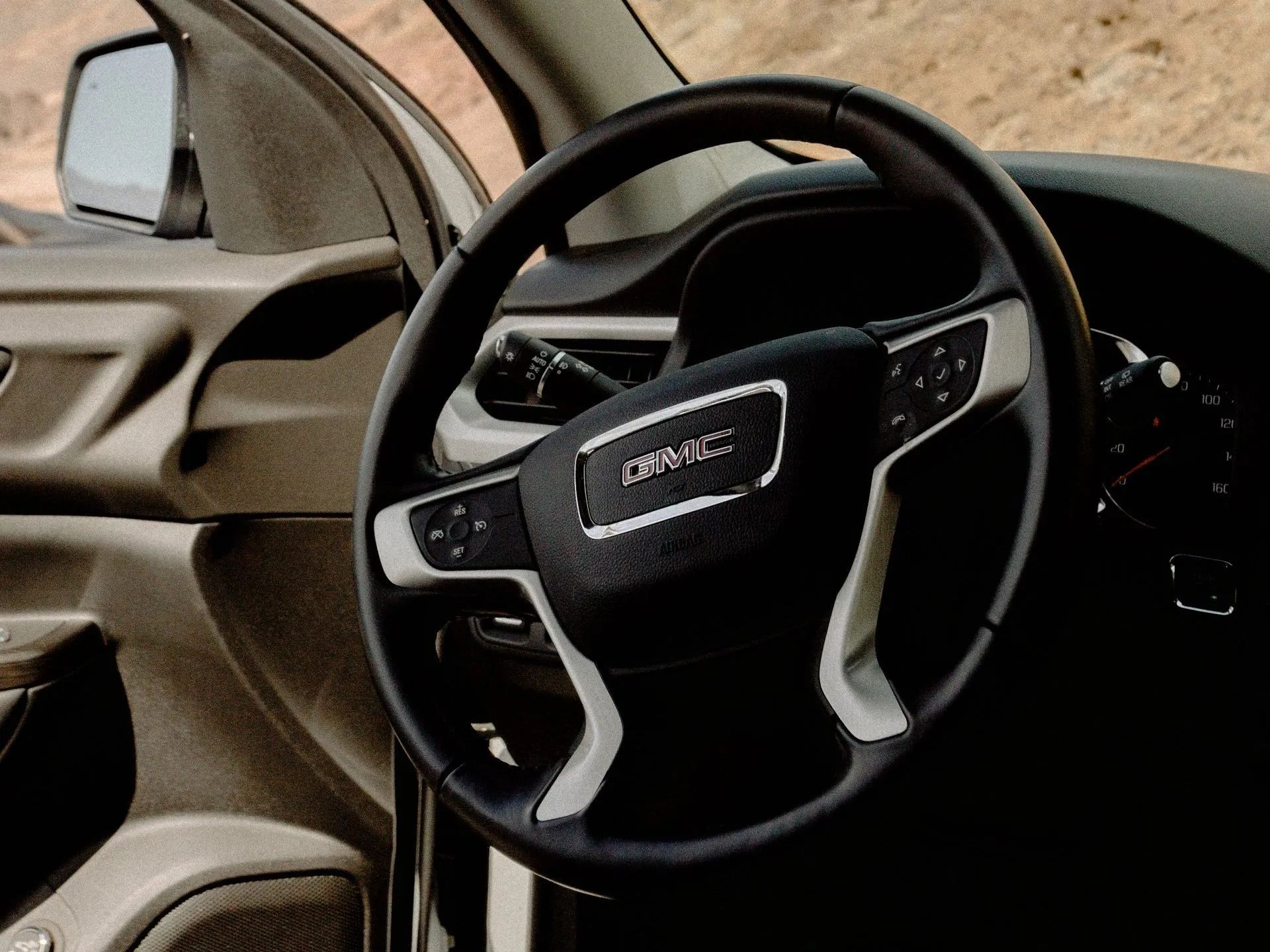 Black and gray GMC steering wheel with controls, inside a vehicle.
