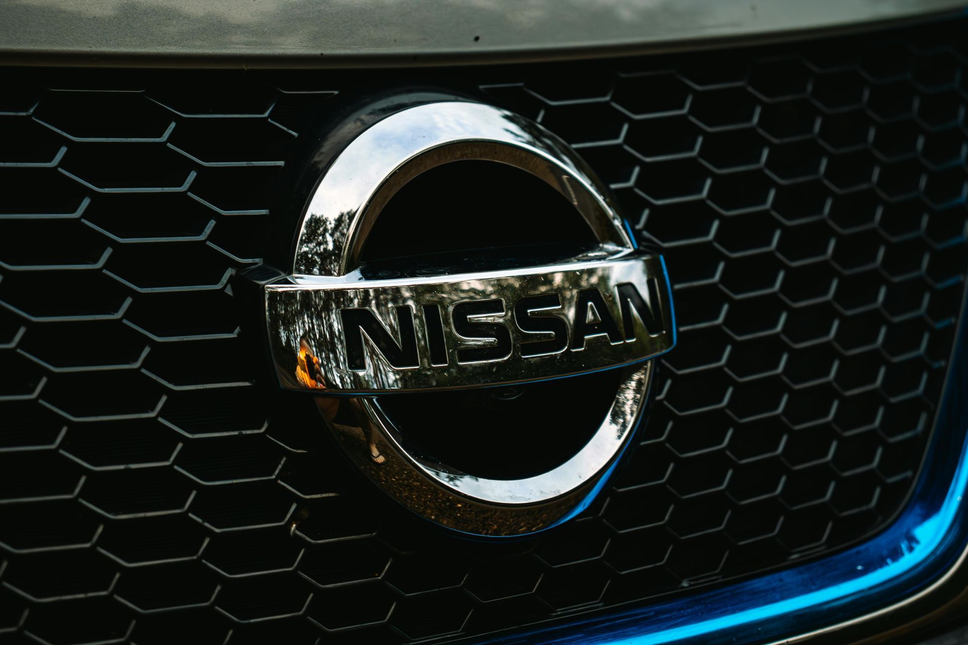 Chrome Nissan emblem on a black hexagonal grille, with blue accents.