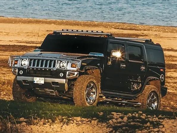 Black Hummer SUV parked on a sandy hill with water in the background.