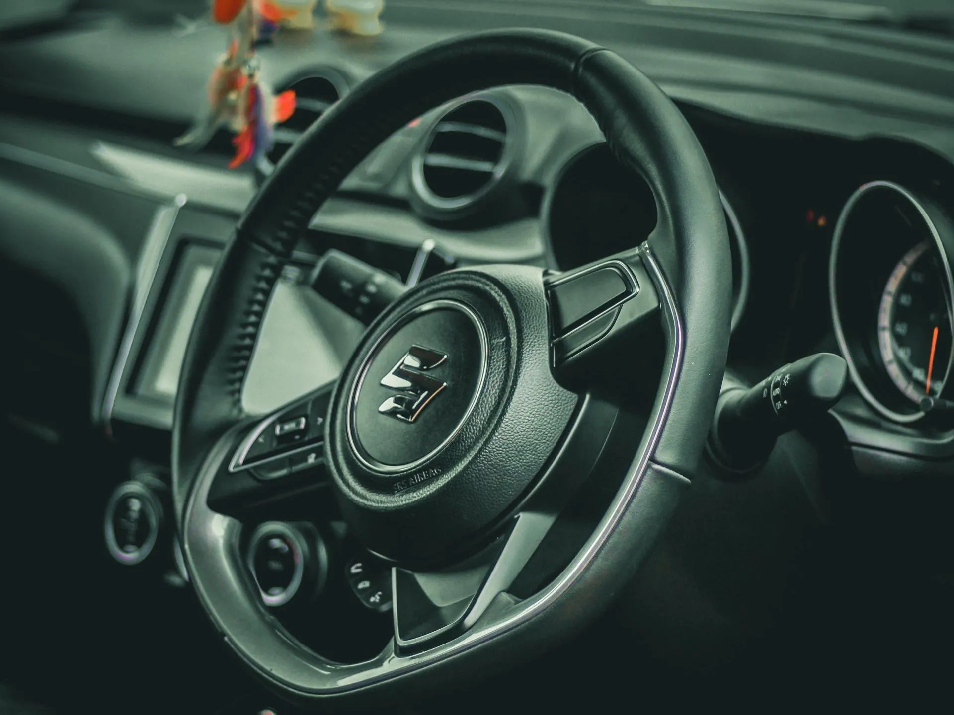 Black Suzuki car steering wheel with white stitching, dashboard visible.