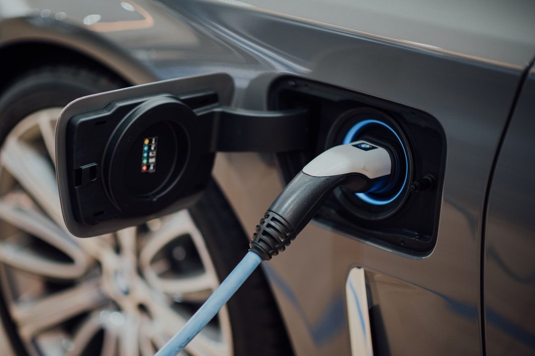 Electric vehicle charging port with charging cable plugged in; blue light around the port.