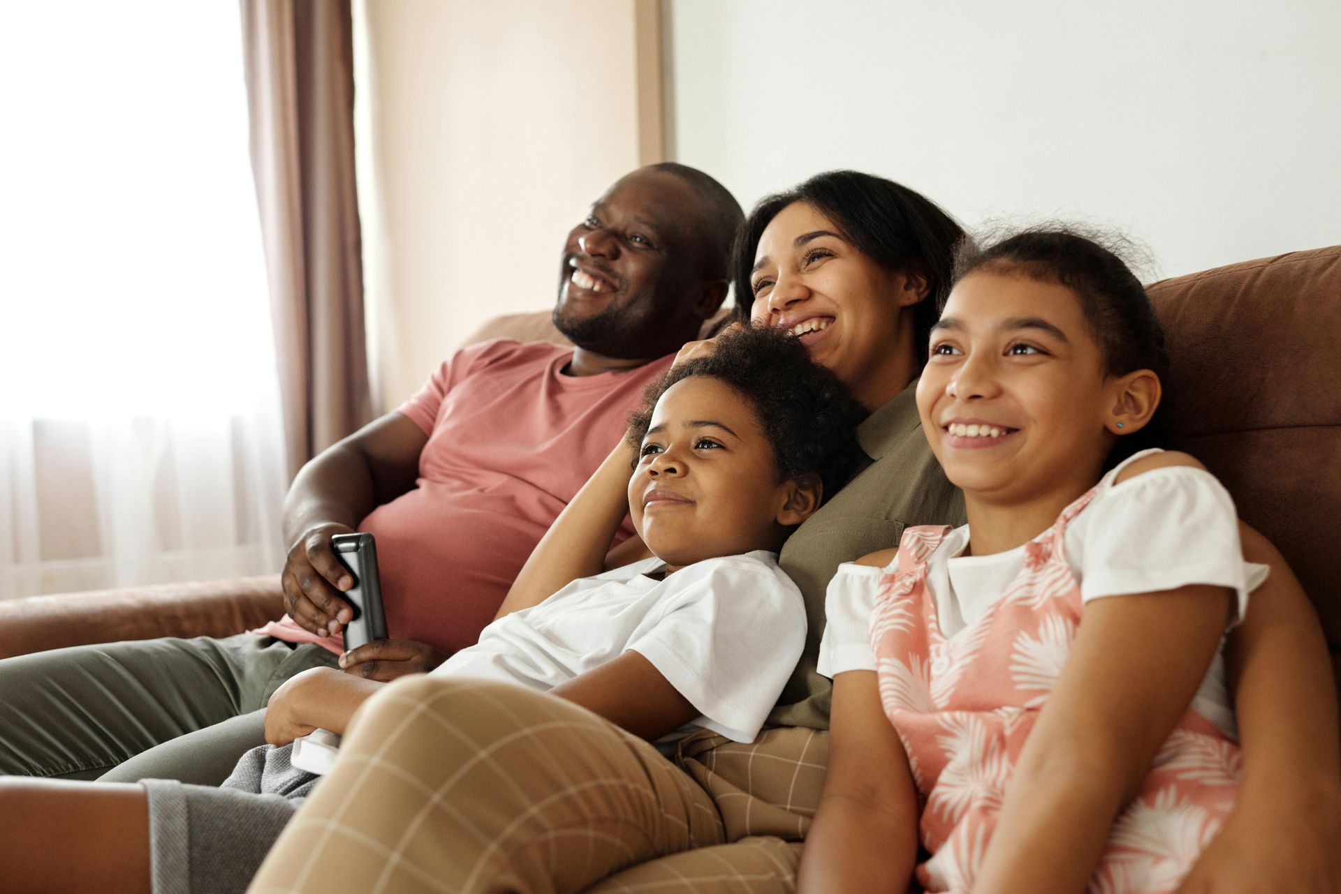 Family of four on a couch, smiling while watching TV.