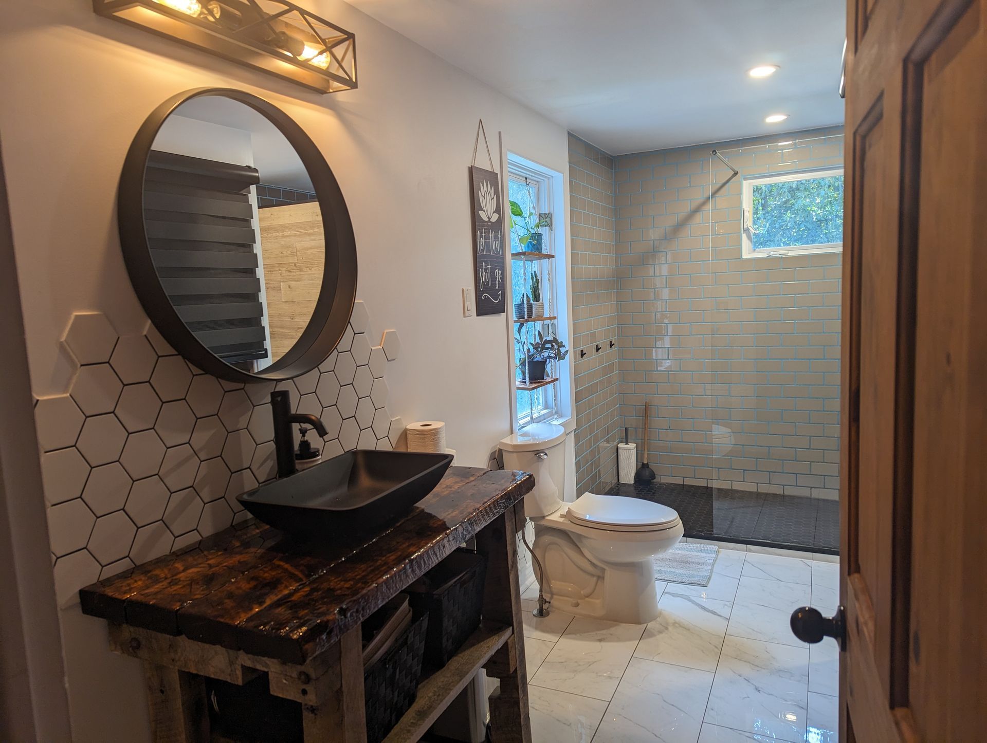 Salle de bains moderne avec murs en marbre, miroir rond, éclairage noir, lavabo blanc et rangements noirs.