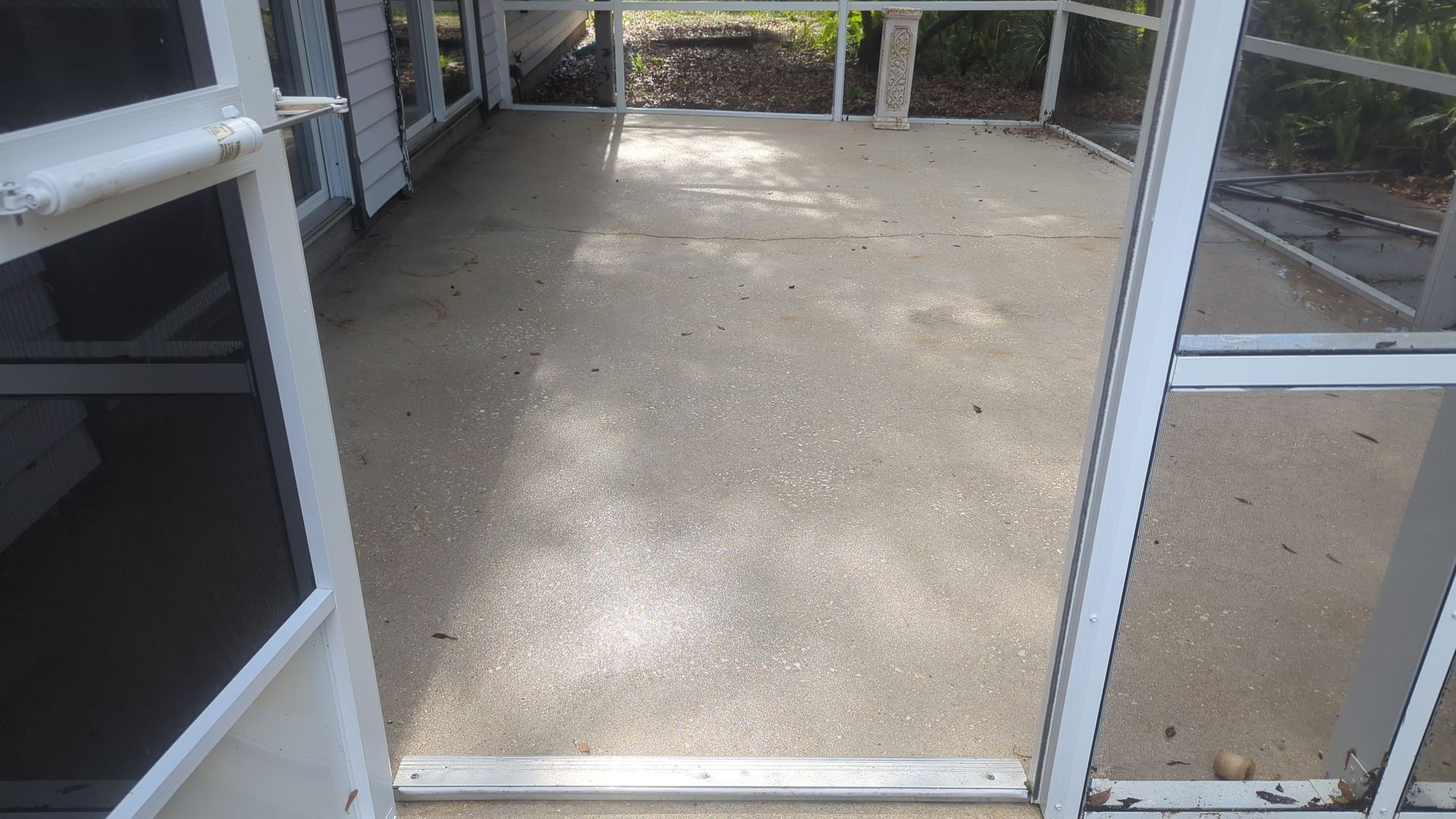 A view through a white screen door looking out onto an empty, light-colored concrete screened-in porch.