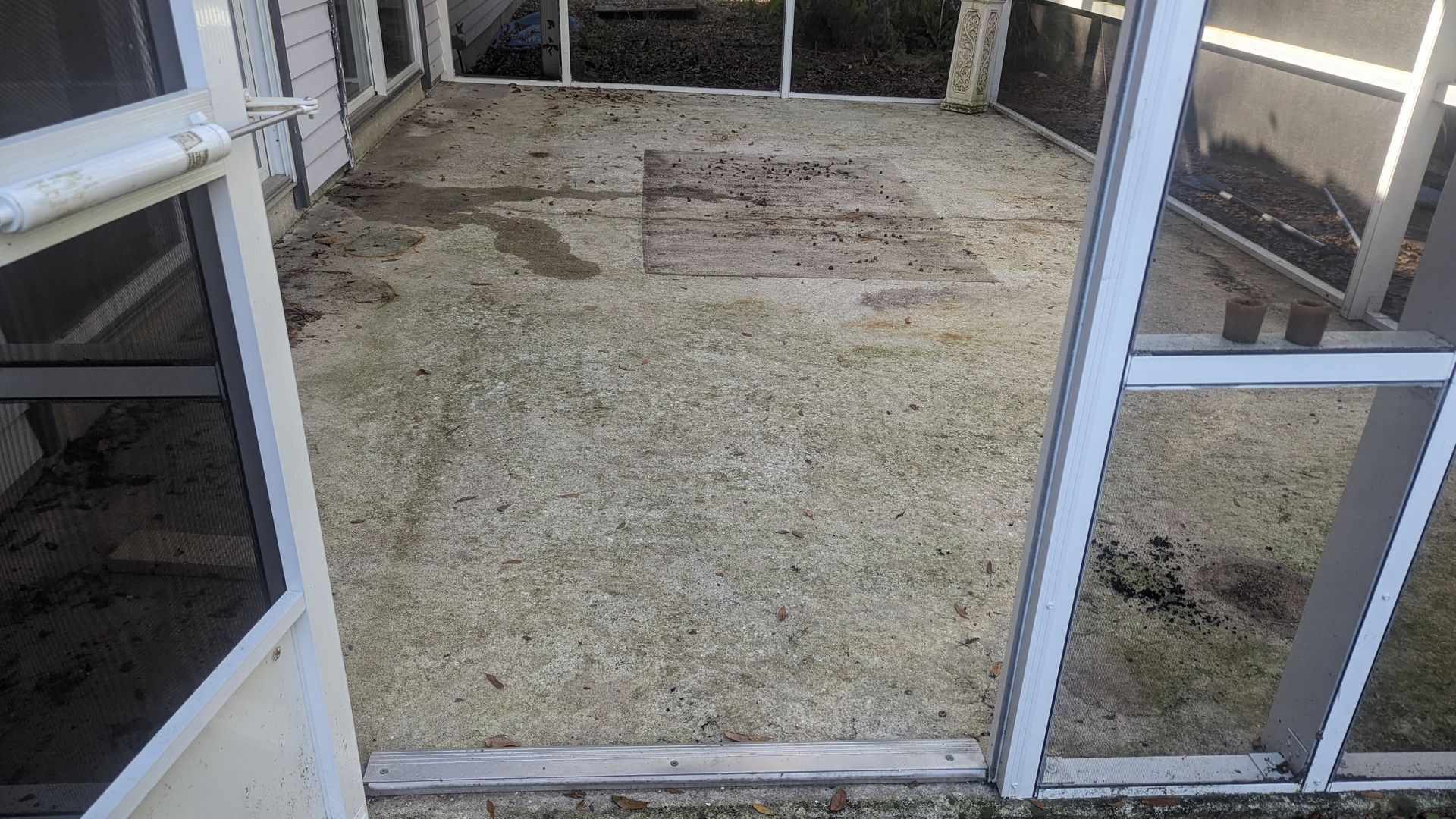 An outdoor screened-in porch with a concrete floor, showing some wear and discolored patches.