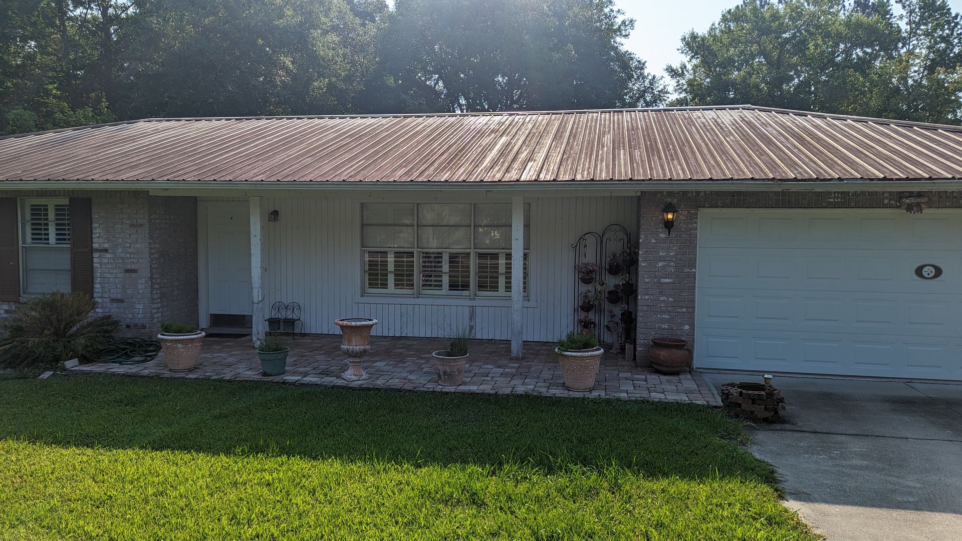 A single-story house with a metal roof, white siding, stone accents, and a garage, featuring a front lawn and rock garden.