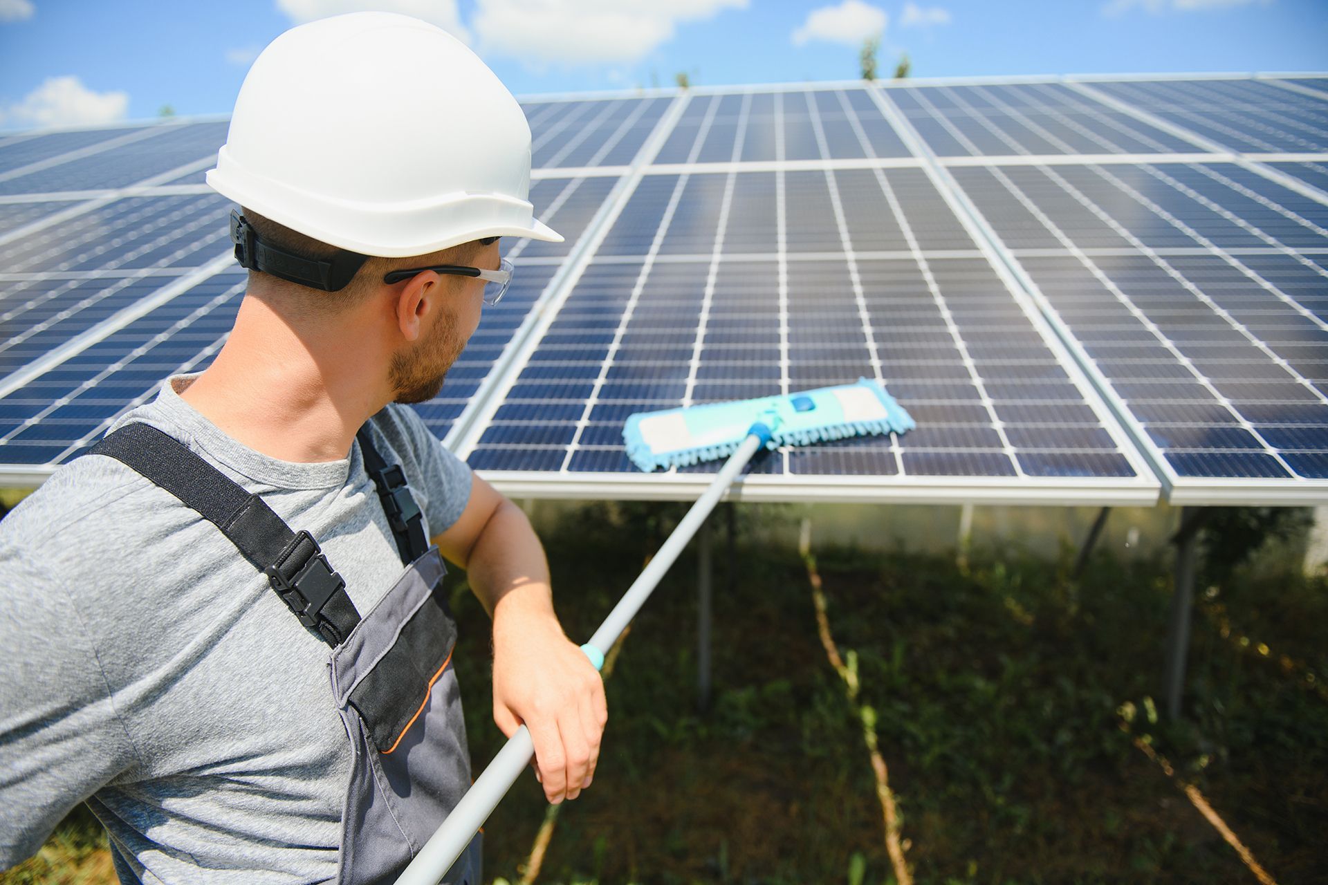 A cleaning tool with a squeegee head being used to wash a dark-colored solar panel.