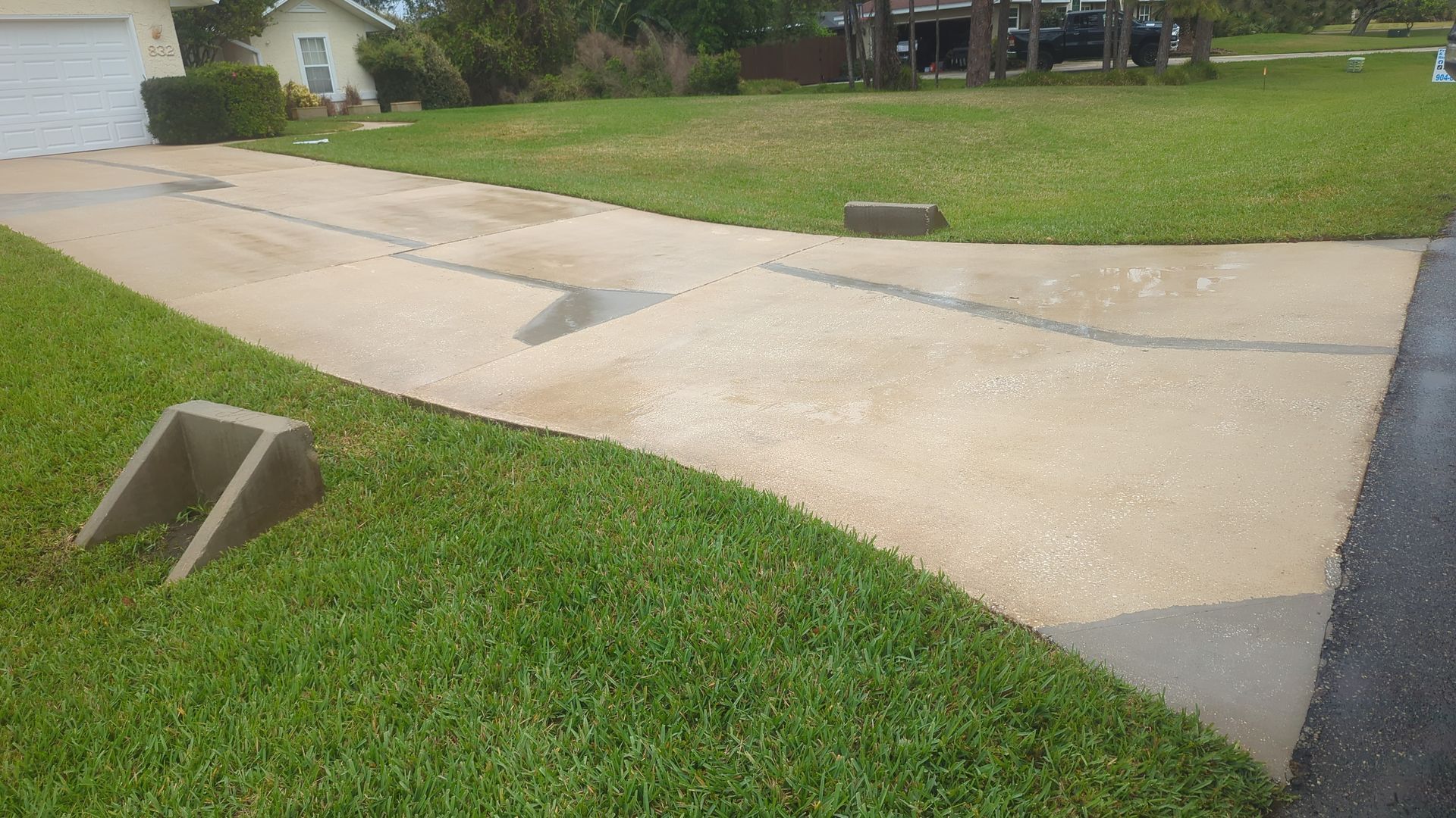A concrete driveway with a large crack and two gray, triangular concrete curb ramps positioned on the grass.