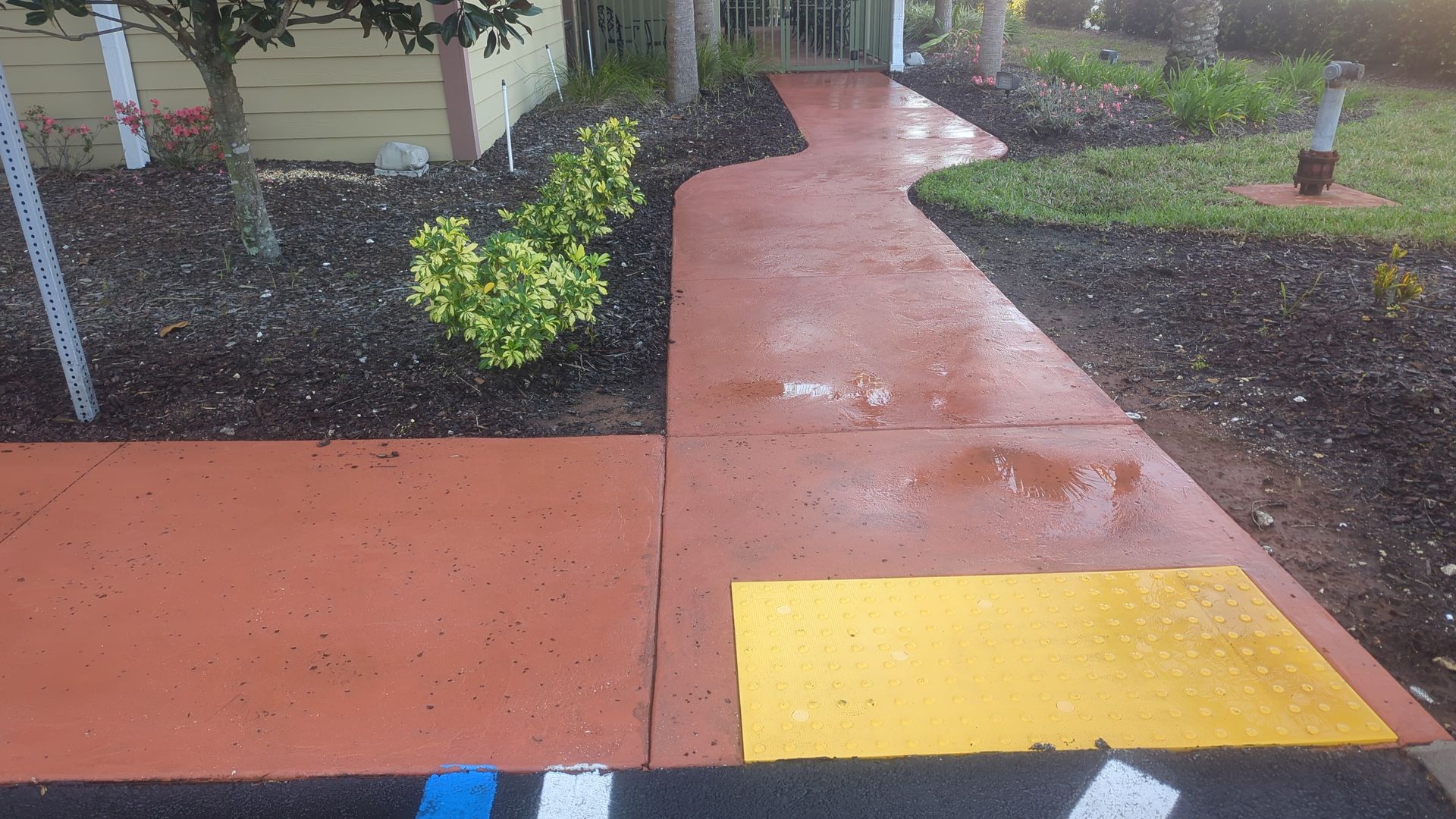 A red concrete walkway leads toward a building, featuring a yellow tactile warning surface at its entrance.
