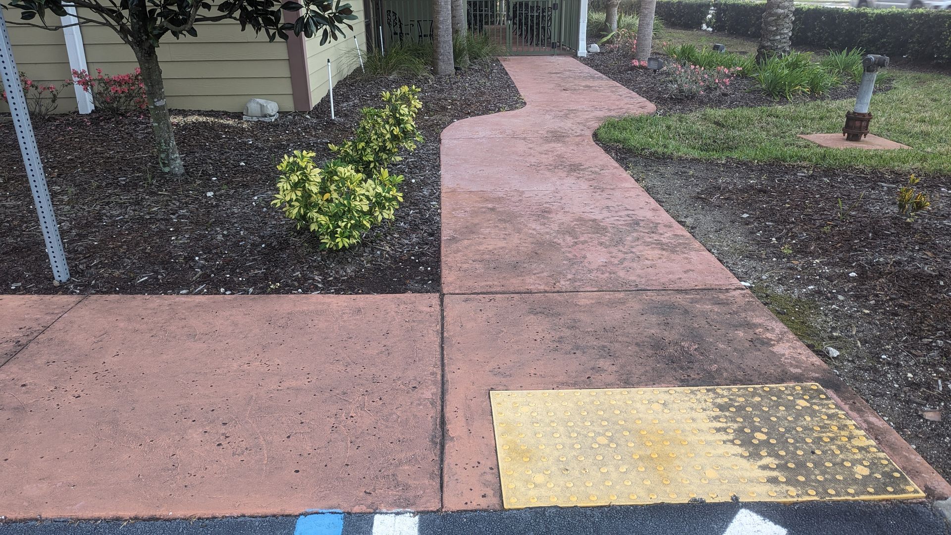 A red concrete walkway transitions into a yellow tactile paving pad, leading toward a building entrance.