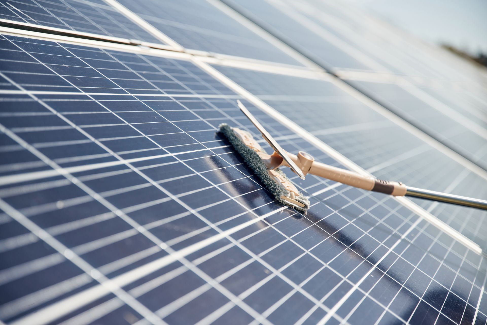 A cleaning tool with a squeegee head being used to wash a dark-colored solar panel.