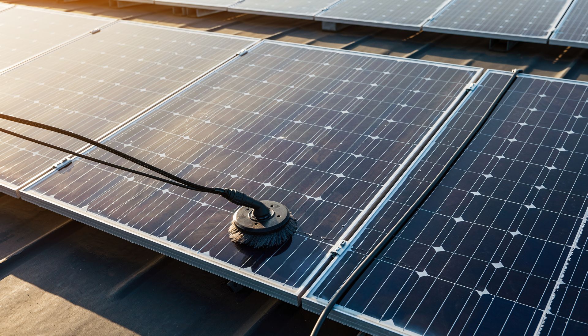 A black cleaning brush attached to a hose on a solar panel on a rooftop.