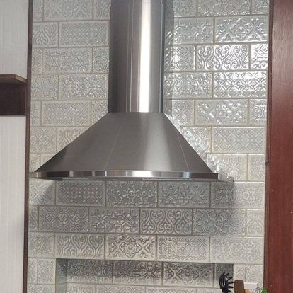 A stainless steel hood is mounted to a brick wall in a kitchen.