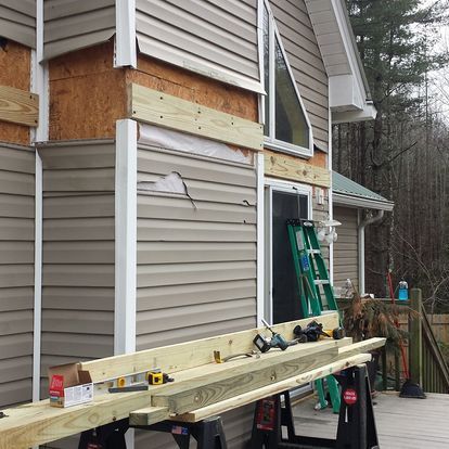 A house is being remodeled with wooden beams and a ladder.