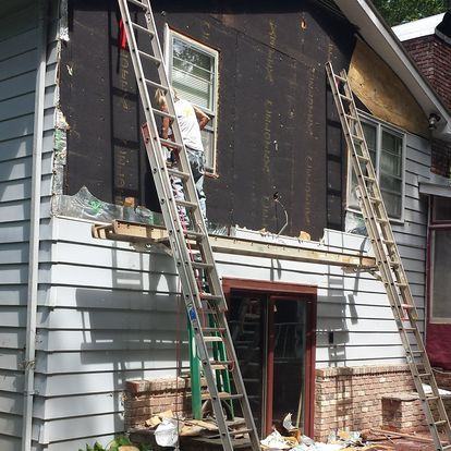 A man on a ladder is working on the side of a house