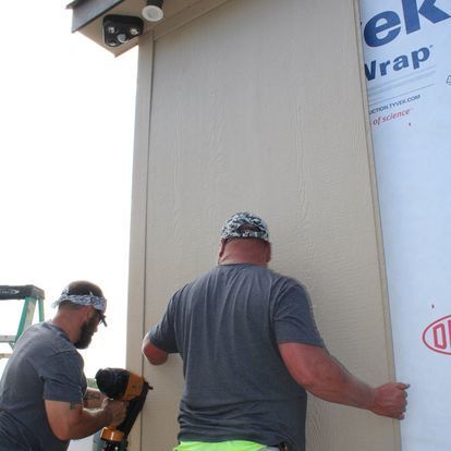 Two men are working on a wall with ek wrap on it