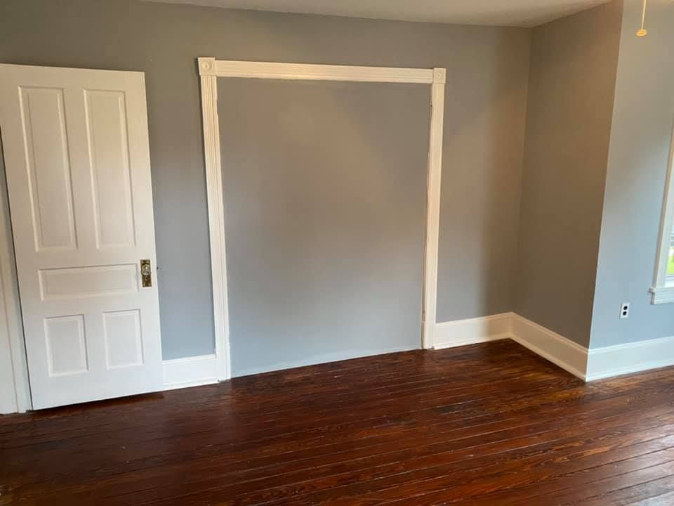 An empty room with wooden floors and gray walls.