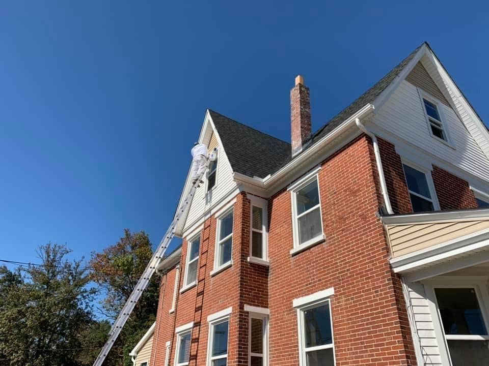 A man on a ladder is painting the side of a brick house.