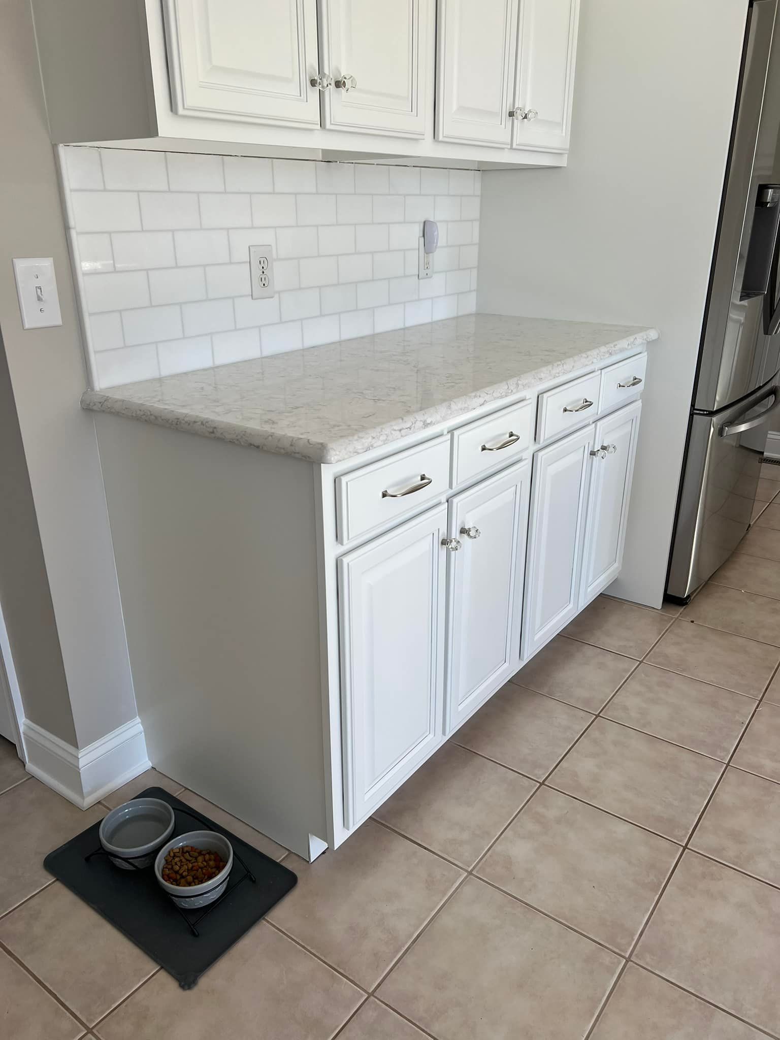 A kitchen with white cabinets and a dog bowl on the floor.