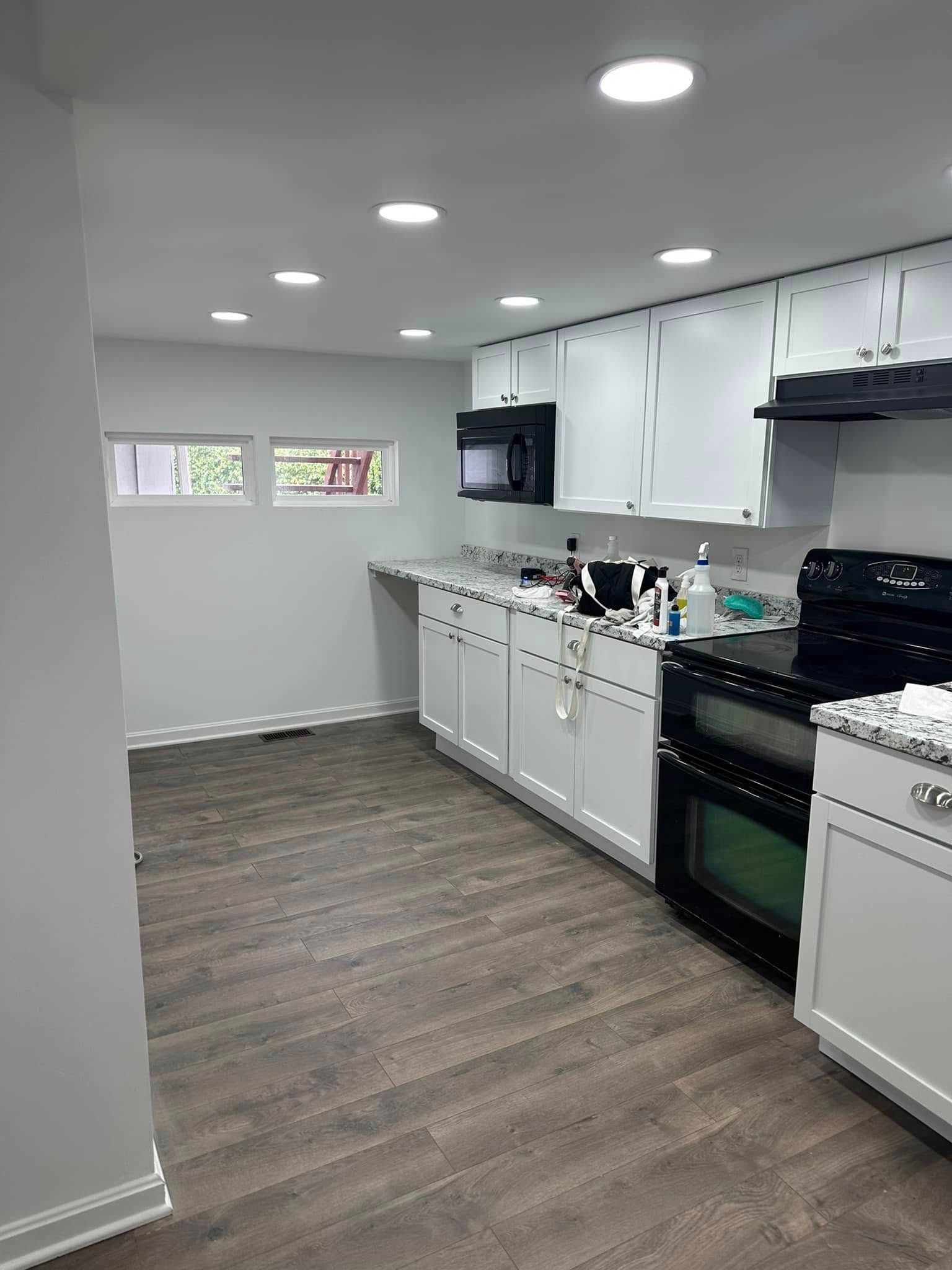 A kitchen with white cabinets , a black stove , a microwave , and a window.