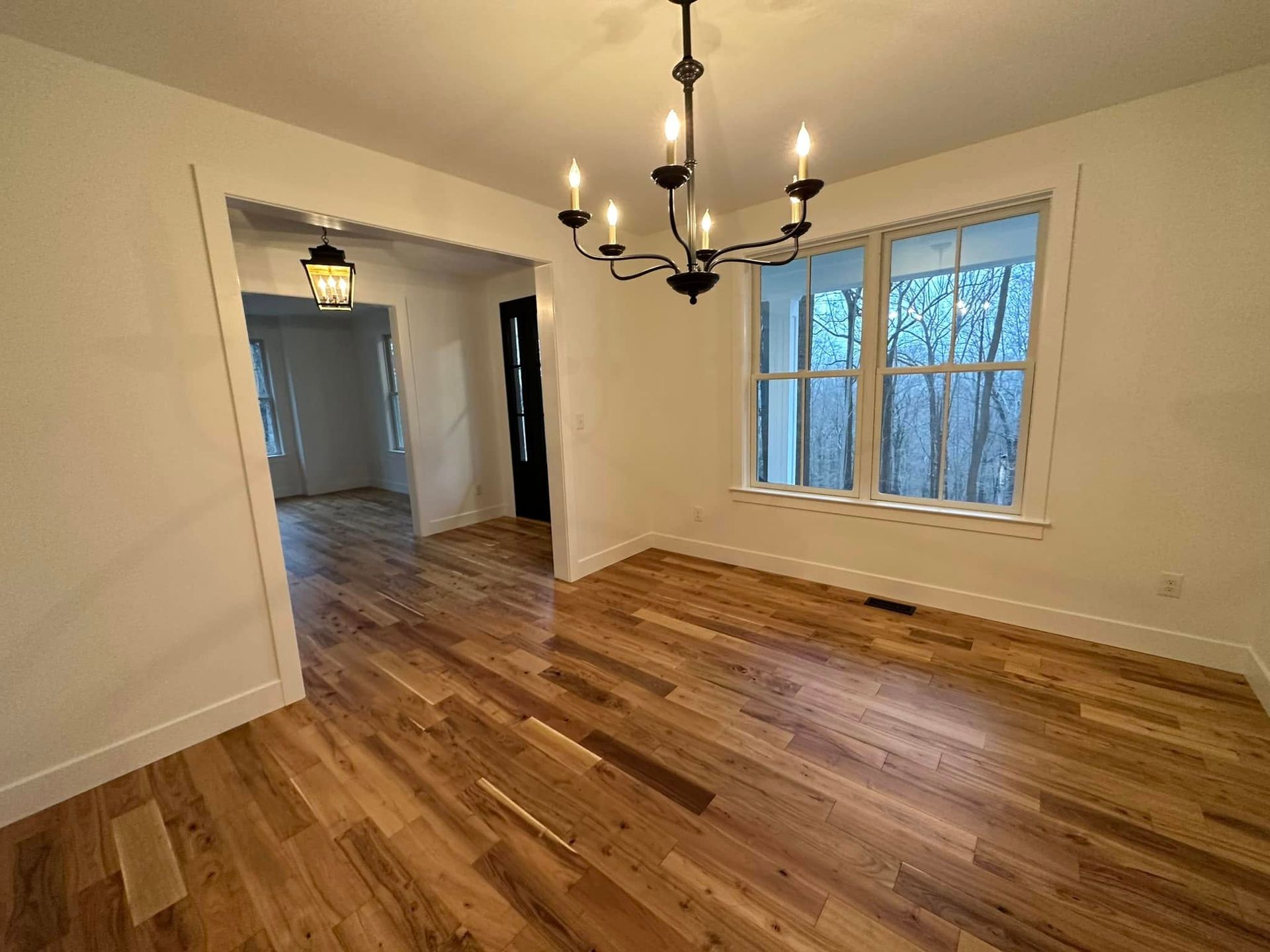 An empty dining room with hardwood floors and a chandelier.