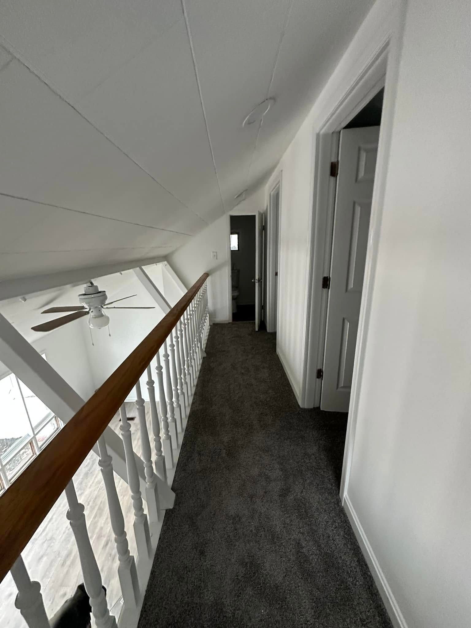 A long hallway with a railing and a ceiling fan in a house.