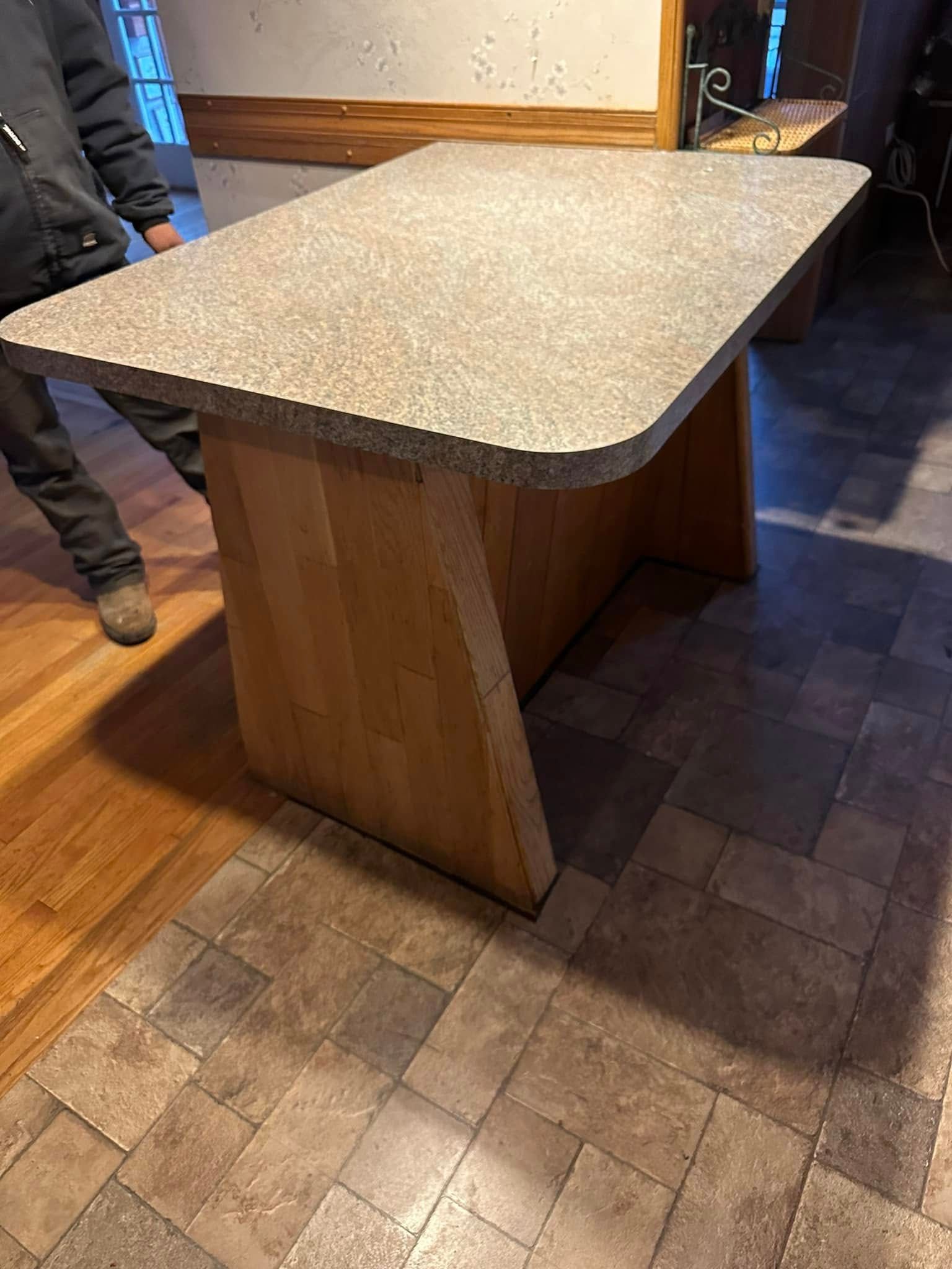 A person is standing next to a wooden table with a granite top.
