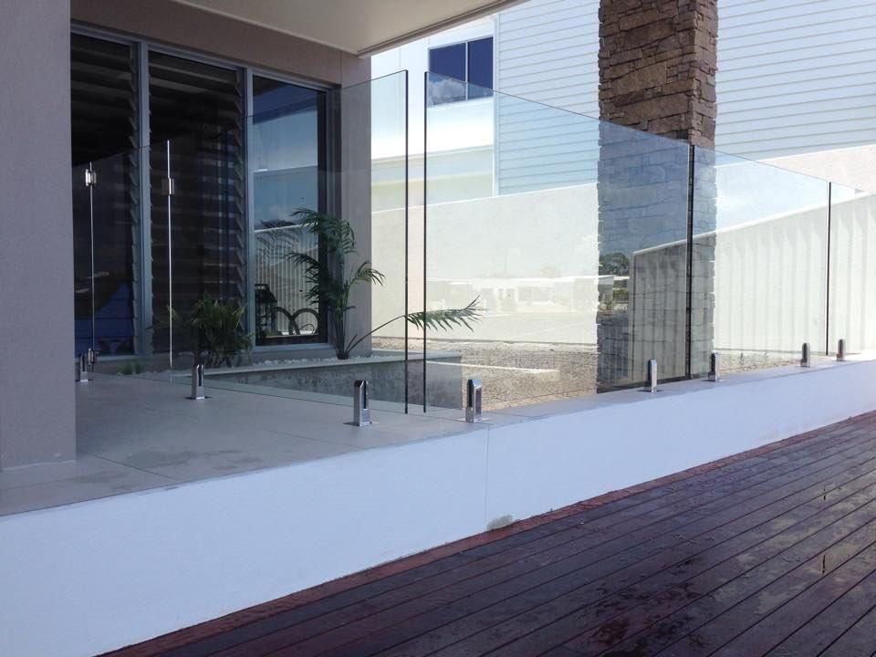 A Glass Railing On A Deck Next To A Building — Frameless Shower Installations In Maroochydore, QLD
