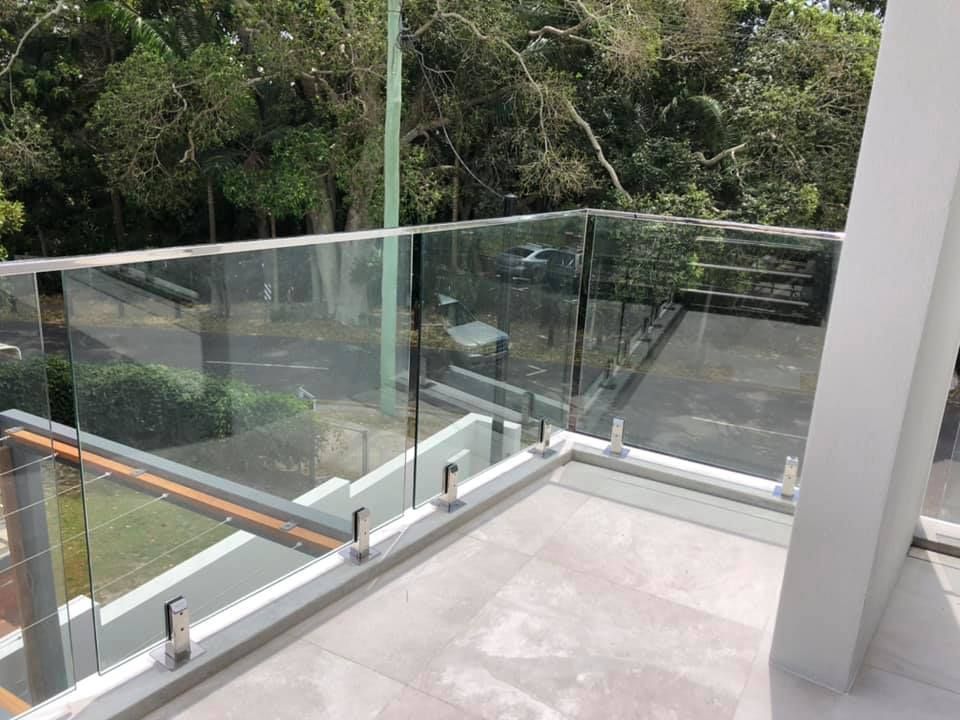 A Balcony With a Glass Railing and Trees in the Background — Frameless Shower Installations In Maroochydore, QLD 