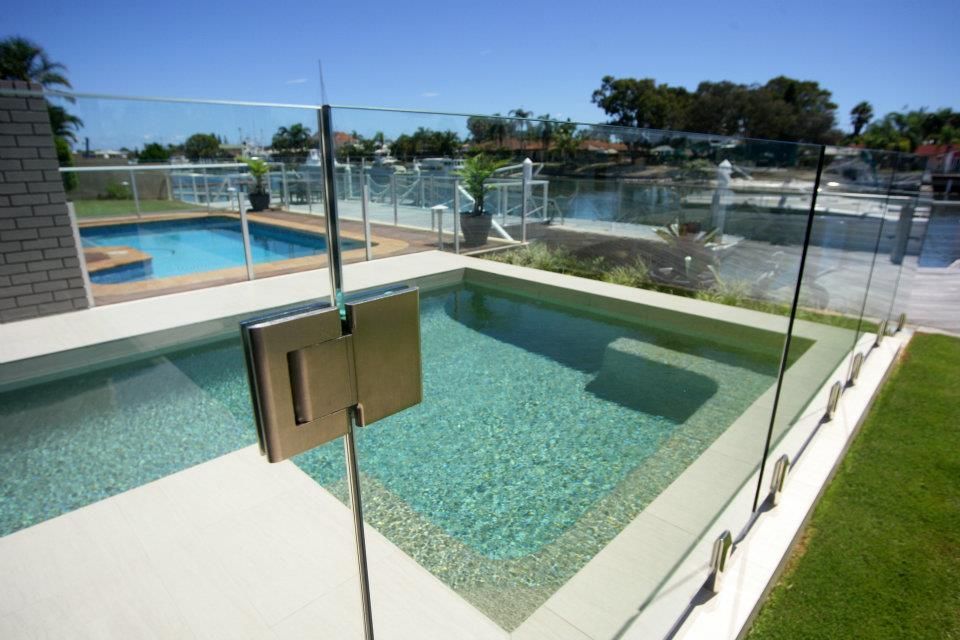 A Swimming Pool With A Glass Fence Around It — Frameless Shower Installations In Caloundra, QLD