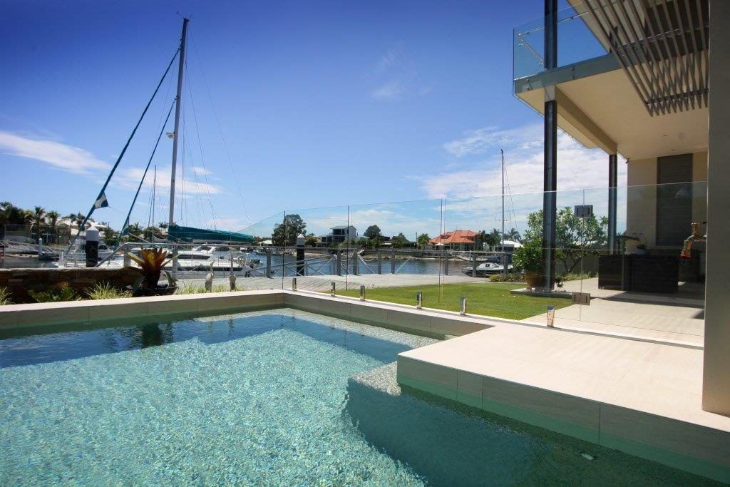A Large Swimming Pool In Front Of A House With A Boat In The Background — Frameless Shower Installations In Maroochydore, QLD