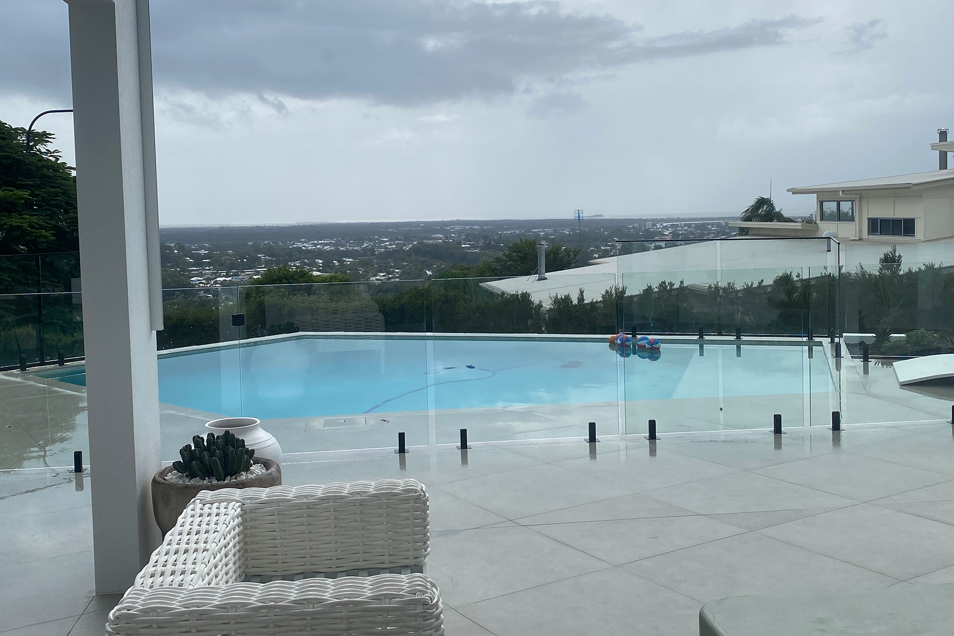 Modern outdoor pool area with frameless glass fencing overlooking a suburban landscape