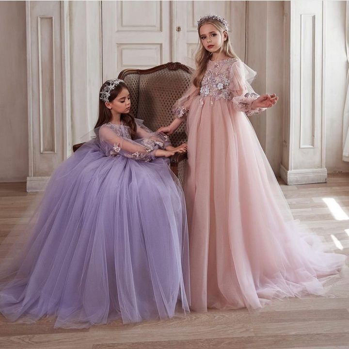 Two little girls in dresses are standing next to each other in a room.