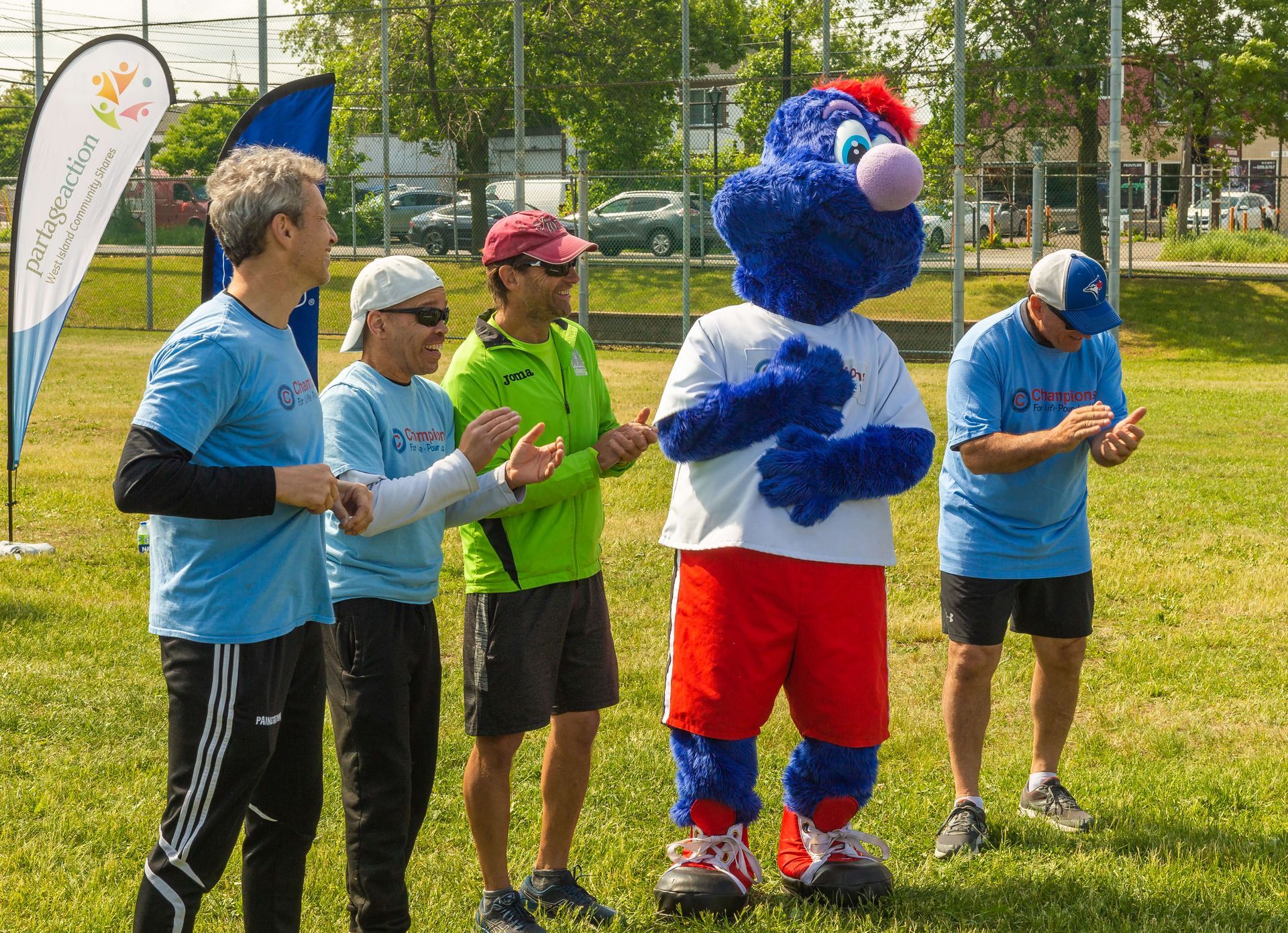 A group of men are standing around a blue mascot.