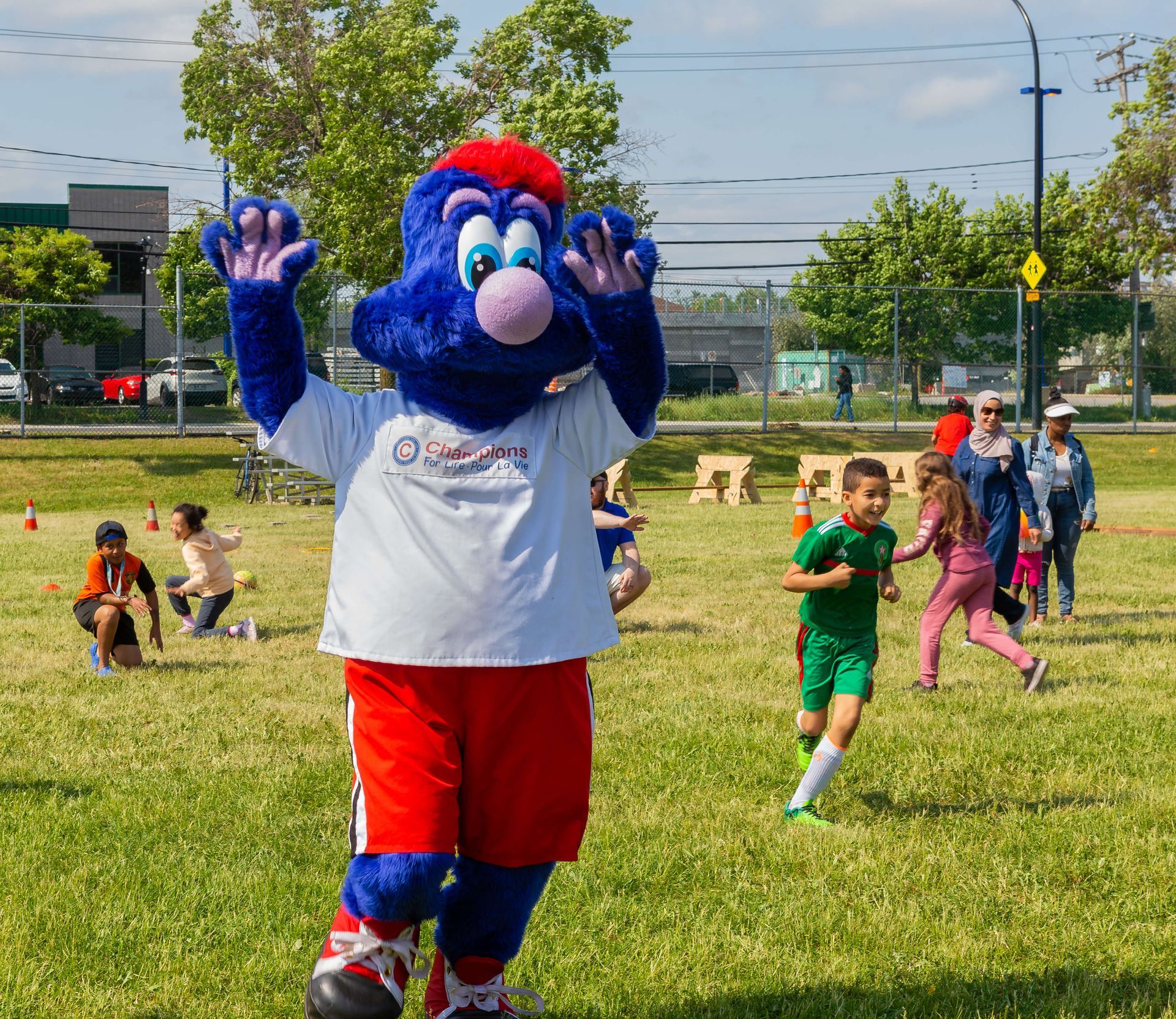 A blue and red mascot is standing in a grassy field