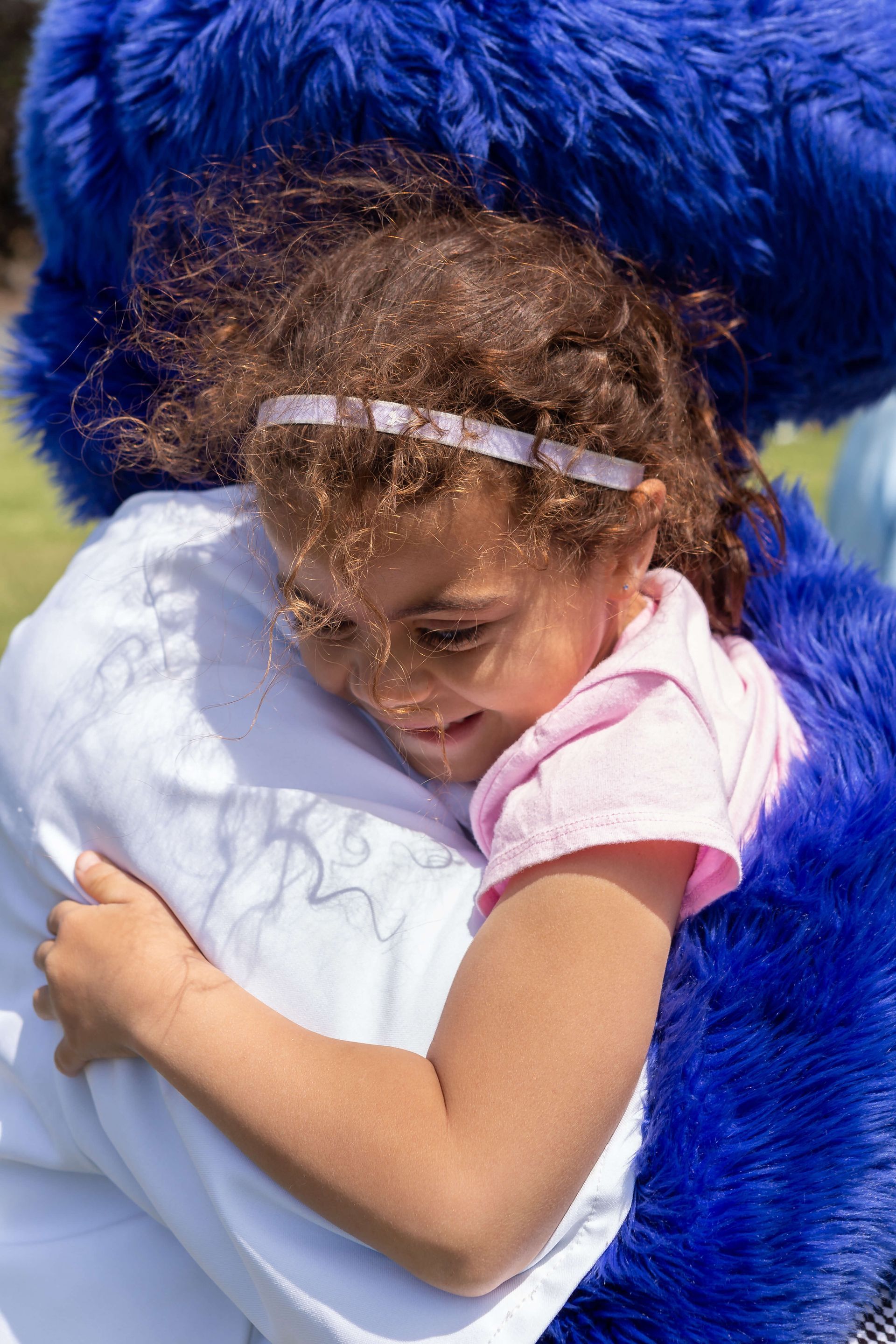 A little girl is hugging a blue stuffed animal.