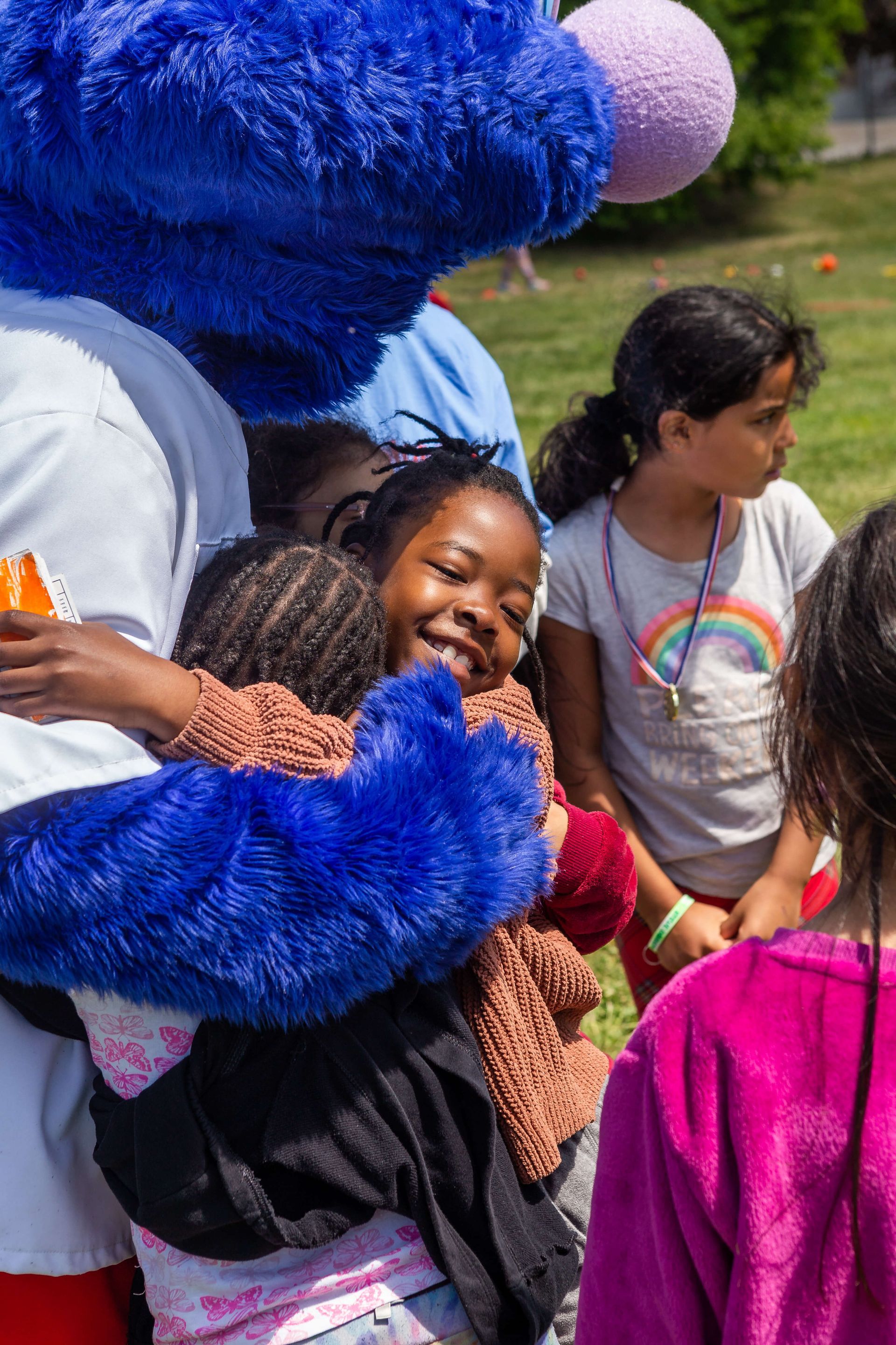 A group of children are hugging a blue sesame street mascot.