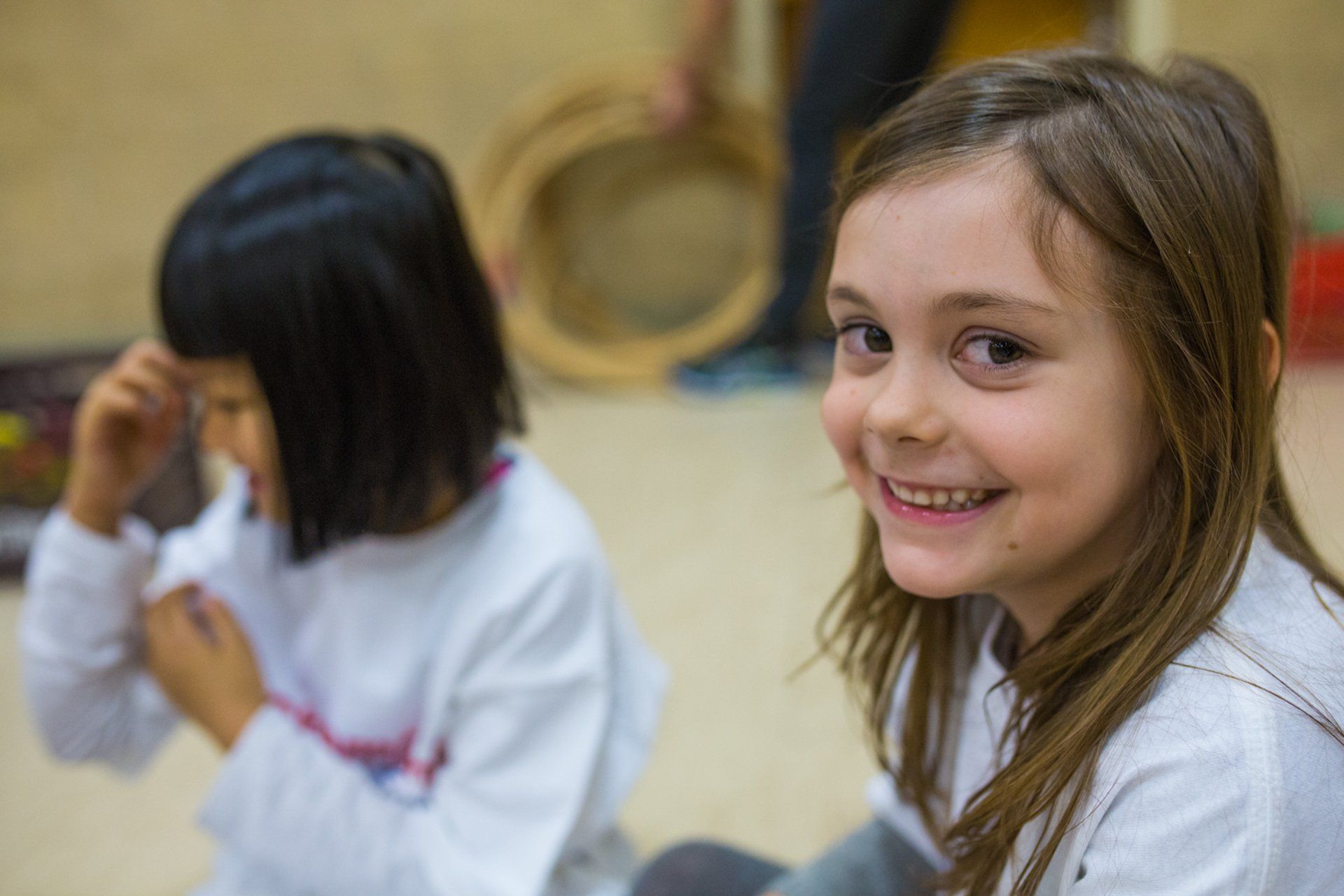 Two young girls are sitting on the floor and smiling for the camera.