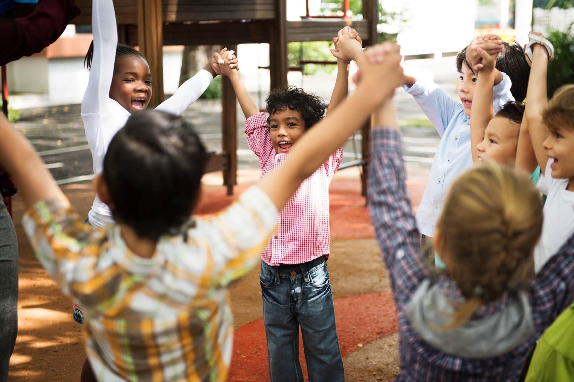 A group of children are holding hands in a circle in a playground.
