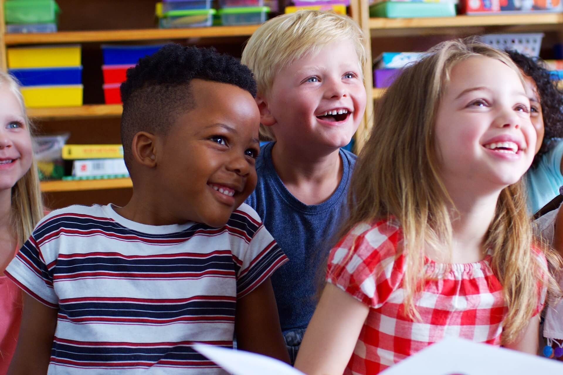 A group of happy children sit in a classroom, engaged in positive learning behaviour