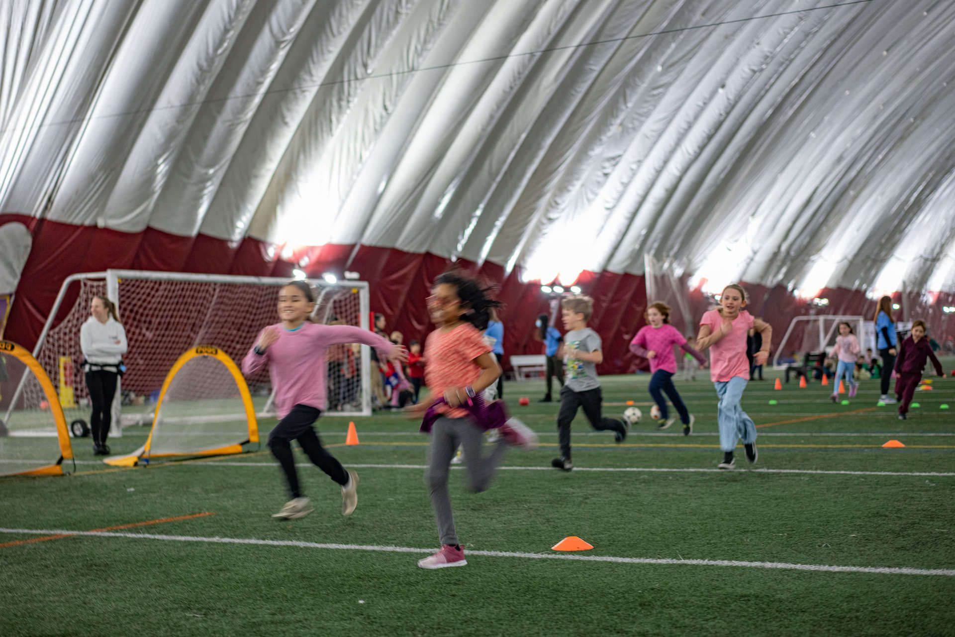 A group of children are running on a field in an indoor gym.