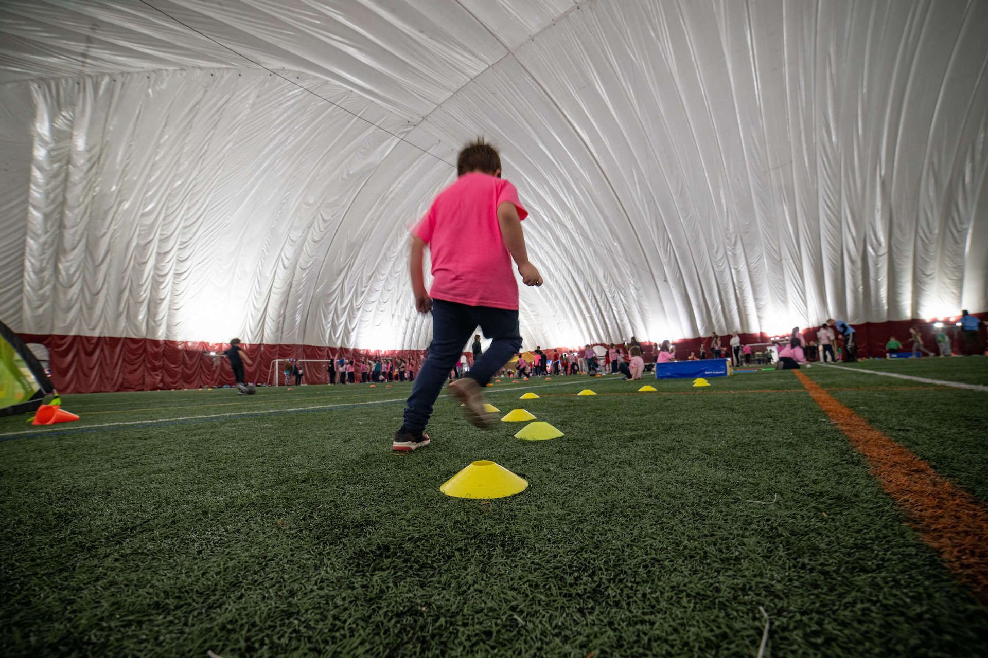 A girl in a pink shirt is running through cones on a field.