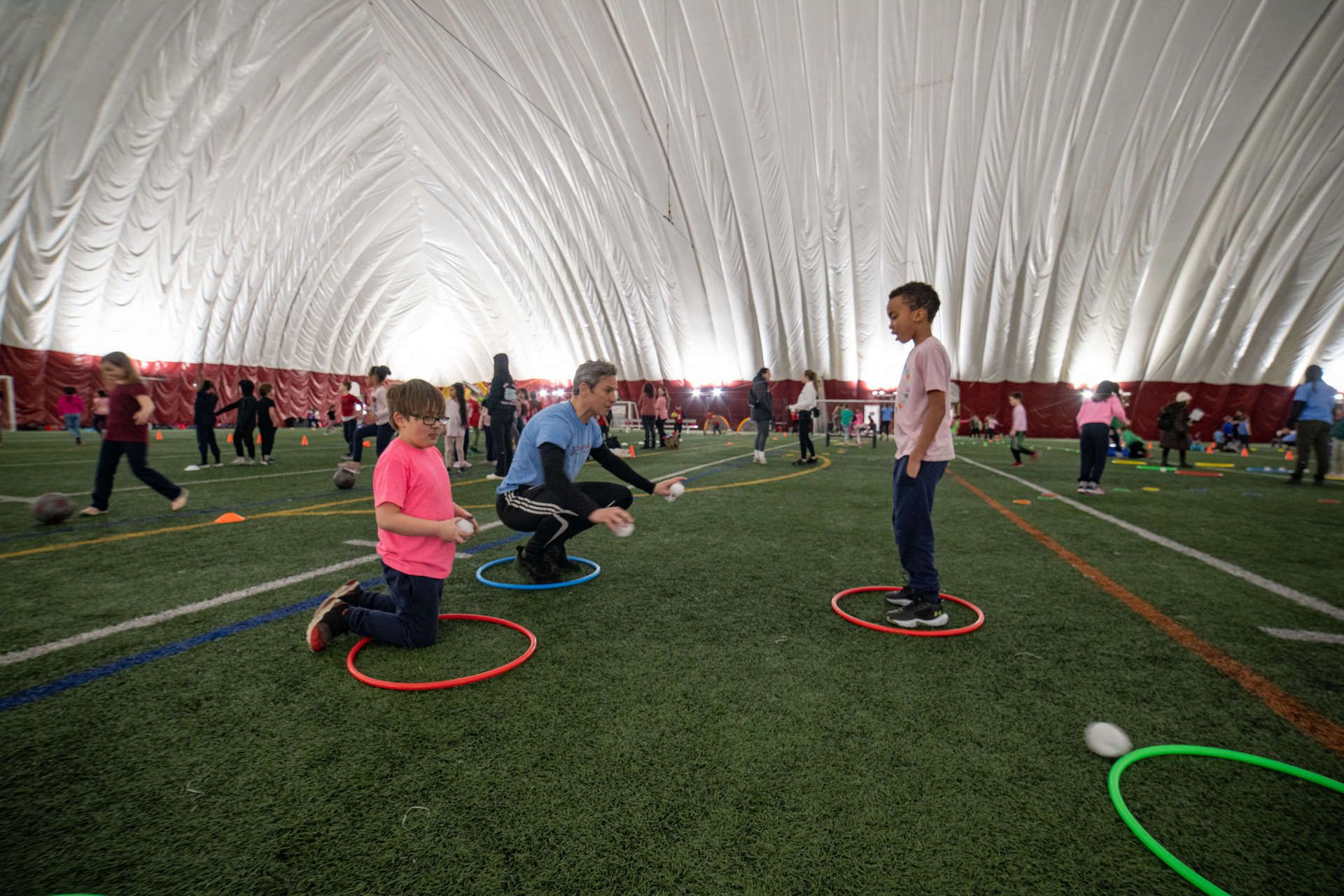 A group of children are playing with hula hoops in an indoor stadium.