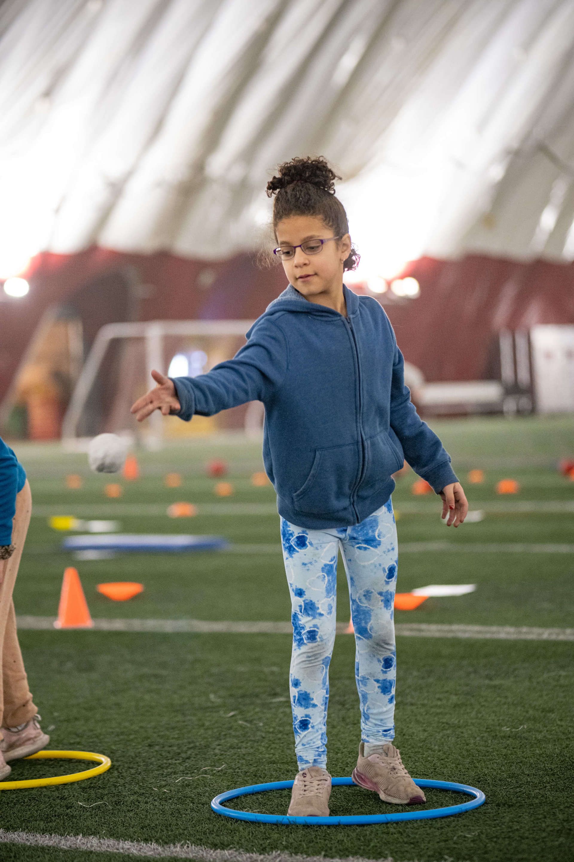 A young girl is standing on a hula hoop on a field.