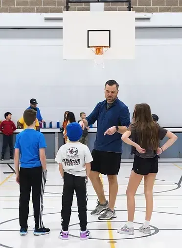 A man is talking to a group of children on a basketball court.