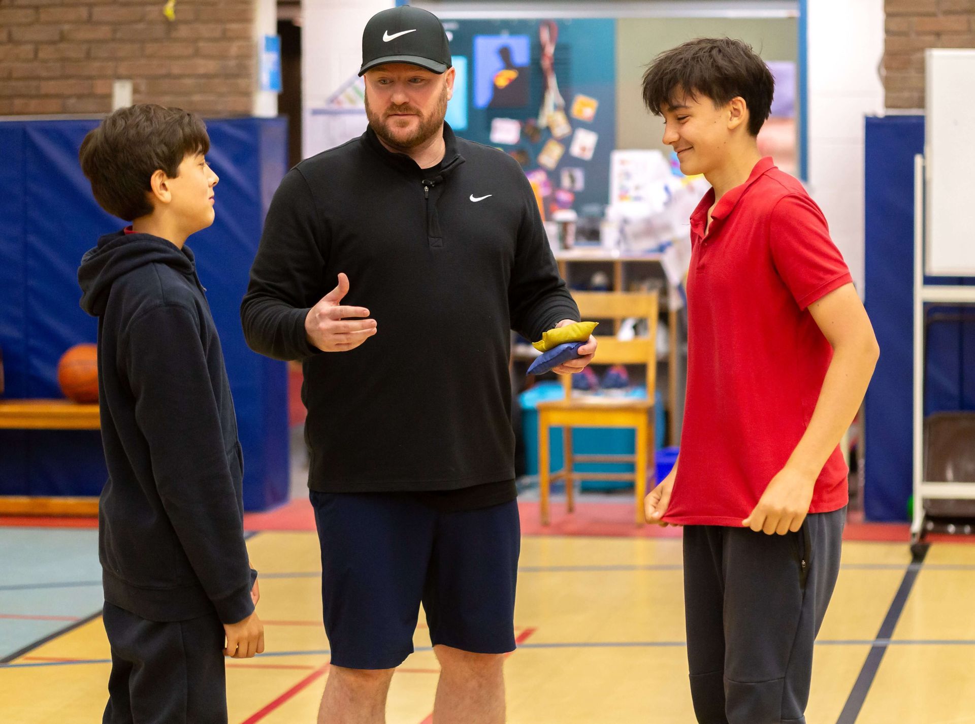 A man is talking to two young boys in a gym.